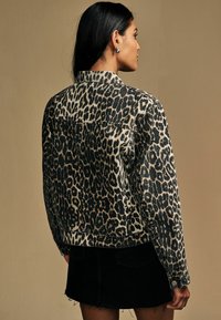 Leopardenmuster-Denimjacke mit lässiger Passform, Knopfverschluss, klassischem Kragen und Gesäßtaschen, kombiniert mit einem schwarzen Rock.