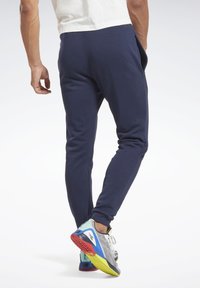 Mørkeblå sweatpants med en tapered design, blød tekstur og sidelommer, parret med multicolore atletiske sko med en mønstret sål.