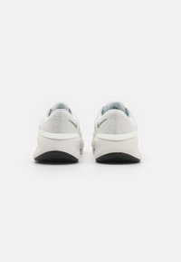 Scarpe da ginnastica grigio chiaro con tessuto testurizzato, colletto imbottito, branding sottile e suola in gomma nera a contrasto.