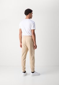 Beige joggerbyxor med smal passform, elastisk midja och bakficka, matchat med en vit t-shirt och vita sneakers.