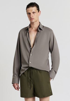 Helles graues Langarmshirt mit Knopfleiste, kombiniert mit strukturierten olivgrünen Shorts mit elastischem Bund.