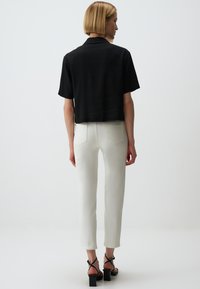 Czarny krótki t-shirt z krótkim rękawem w stylu cropped, w połączeniu z białymi dobrze dopasowanymi spodniami oraz czarnymi sandałami na słupku. Prosty design i lekka tkanina.
