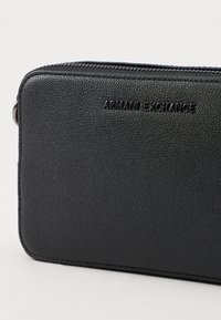 Juodas tekstūruotas odinis piniginė su užtrauktuku ir iškilniu "Armani Exchange" logotipu priekyje. Lygaus paviršiaus, su suapvalintais kraštais.