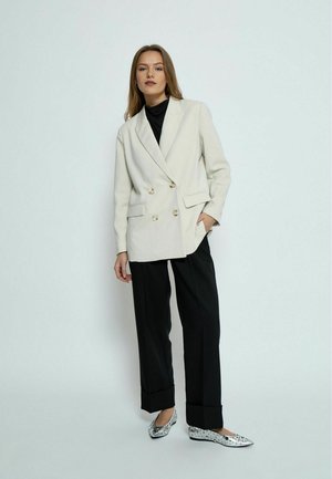 Dubbelzijdig crèmekleurig blazer met gouden knopen, gecombineerd met zwarte wijde broek en zilver versierde flats. Gladde stof en op maat gemaakt pasvorm.