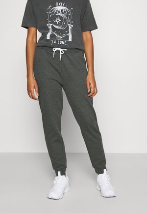 Person iført mørkegrå joggingbukser med hvid snor, hvide sneakers og en matchende mørkegrå T-shirt med en grafik af måne og stjerner med teksten "LA LUNE".