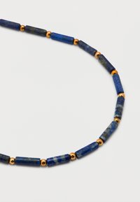 Κολιέ με κυλινδρικές μπλε πέτρινες χάντρες και μικρές στρογγυλές χρυσές χάντρες που εναλλάσσονται σε ένα ανοιχτό φόντο.
