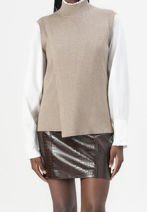 Woman wearing beige sleeveless knit vest over white long-sleeve blouse paired with dark brown crocodile-patterned leather mini skirt.