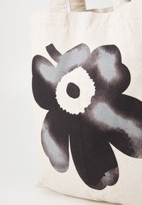 Cotton tote bag featuring a large black flower with gray accents on a beige background. Includes sturdy fabric handles.