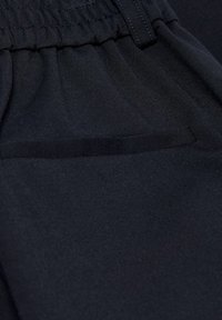 Černé tkané kalhoty s elastickým pasem, s jemnou strukturou a jednou náprsní kapsou na přední straně.