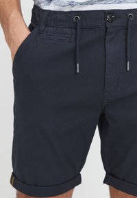 Pantaloni corti in cotone blu navy con chiusura a cordoncino, tasche laterali e orli risvoltati. Caratterizzati da una chiusura con bottone e dettagli di cucitura sottili.