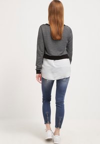 Haut rayé noir et blanc avec une ceinture noire, associé à un jean bleu slim avec des ourlets fendus. Porté avec des baskets blanches.