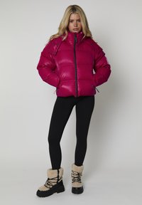Fuksjowa puchowa kurtka z zapięciem na zamek, elastycznymi mankietami i bocznymi kieszeniami, w połączeniu z czarnymi legginsami i kremowymi butami z futrzanym wykończeniem.