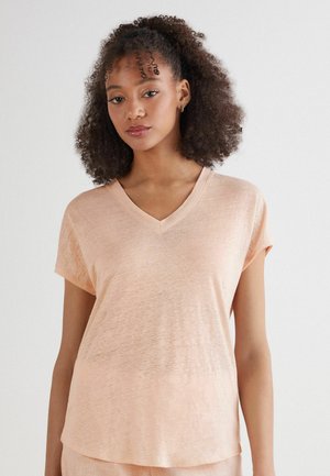 Korte mouwen, lichtgewicht V-hals top in een zachte perzik kleur, met een relaxte pasvorm en subtiele textuur. Geen opvallende patronen of accenten.
