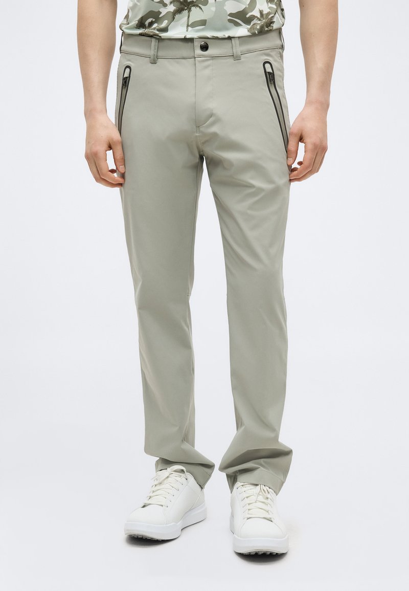 Homme portant un pantalon droit gris clair avec des poches avant zippées noires et des baskets blanches.
