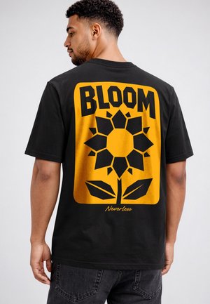 Man wearing black t-shirt with large yellow graphic of a sunflower and the words "BLOOM" and "Nevertheless" on the back.