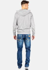 Grijze capuchontrui met een relaxte pasvorm, gecombineerd met middelblauwe denim jeans met decoratieve stiksels en merk-geëtiketteerde achterzakken.