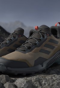 Brown and black hiking shoes with textured fabric, rubber sole, orange accents, and three black stripes on the sides.