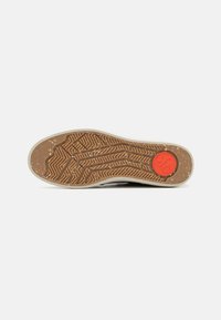 Talpa de sneaker cu un design din cauciuc texturat de culoare maro, prezentând un model unic și un accent circular roșu la călcâi.