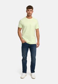 Light green cotton t-shirt on a person, paired with dark blue jeans and white sneakers. Simple design, short sleeves, relaxed fit.