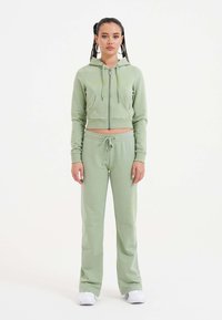 Lichtgroene cropped hoodie met rits en kangoeroezakken, gecombineerd met bijpassende sweatpants met een verstelbare trekkoord tailleband.