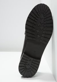 Semelle de chaussure noire avec un motif de bande de roulement profond et robuste incluant des crampons rectangulaires et en forme de croix, avec la taille 37 embossée près de la voûte plantaire.