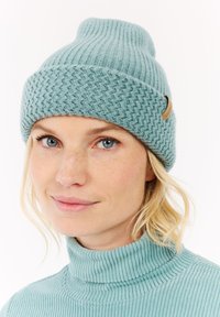 Lichtblauwe gebreide beanie met een gestructureerd patroon en een omgerolde rand, voorzien van een klein leren label aan de zijkant.