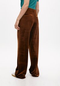 Pantaloni a gamba larga in velluto marrone con vita alta, due tasche posteriori e una texture liscia. Abbinati a sneakers bianche.