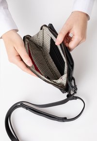 Borsa in pelle nera con chiusura a zip, dotata di un interno grigio a fantasia e più scomparti per carte. È visibile una tracolla removibile.