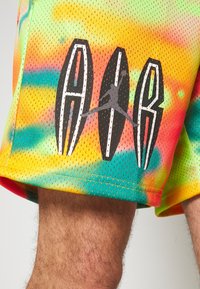 Mesh athletic shorts with a tie-dye pattern in orange, green, and yellow. Features black and white surfboard graphics with a logo accent.