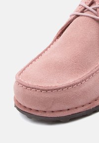 Κοντινή λήψη του μπροστινού μέρους ενός ροζ παπουτσιού από σουέντ με λεπτομερή ραφή και σκούρα λαστιχένια σόλα.