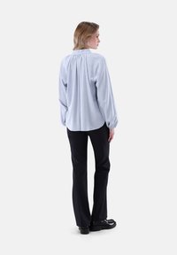Blusa blu chiaro a maniche lunghe con schiena arricciata, abbinata a pantaloni neri. La blusa presenta un collo arrotondato e polsini elasticizzati.