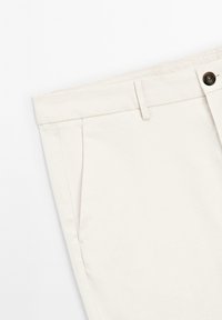 Beige broek met een platte voorkant, zijzakken en een enkele knoopsluiting, gemaakt van lichte stof met een zachte textuur.