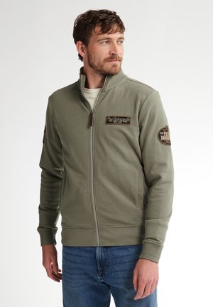 Olive green zip-up jacket in soft cotton blend with ribbed cuffs, two side pockets, and embroidery patches on chest and sleeve.
