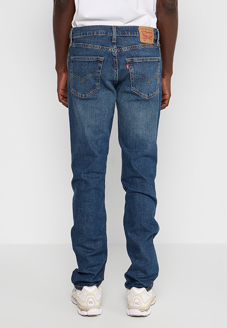 Jean en denim bleu foncé avec une coupe droite, arborant une patch en cuir à l'arrière, des coutures contrastées et deux poches arrière.