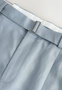 Light blue fabric pants waistband with a metal rectangular buckle and visible white inner lining with black stitching details.
