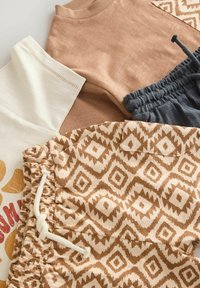 Quatre vêtements : une chemise crème avec un motif graphique, un haut marron clair, un pantalon gris foncé et un pantalon crème avec un motif à losanges marron.