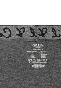 Tessuto grigio con scritte nere. Etichette di cura e contenuto stampate in bianco. Composizione del materiale: 95% cotone, 5% elastan. Taglia: M.