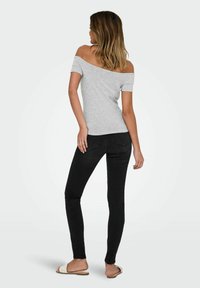 Grå off-the-shoulder t-shirt parret med sorte skinny jeans og hvide slide-sandaler, der fremhæver et enkelt design og tætsiddende silhuet.