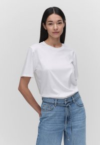 Biała koszulka bawełniana z okrągłym dekoltem i krótkimi rękawami, zestawiona z jasnoniebieskimi spodniami o wysokim stanie z przewiązywanym paskiem.