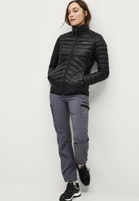 Sort isoleret jakke med høj krave og quiltet design, kombineret med grå cargo bukser med sidelommer og afslappet pasform. Sorte fodtøj.
