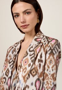 Blazer con paillettes caratterizzato da un motivo astratto multicolore in tonalità di marrone, rosa e blu. Collo a punta e tessuto testurizzato.