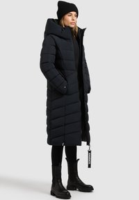 Garšs, pūkains jaka tumši zilos toņos ar ševronu izšuvumu, augsts apkakle, priekšējais rāvējslēdzis un sānu kabatas. Nēsāta virs melna apģērba un potīšu zābakiem.