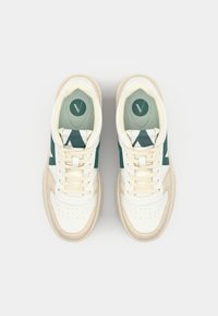 Białe sneakersy mają zielone akcenty, teksturowany język, perforowaną czubek buta i beżową podeszwę. Sznurówki są płaskie i równomiernie rozmieszczone.