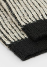 Écharpe tricotée avec des rayures alternées noir et écru, présentant une finition texturée et de subtils fils métalliques tissés tout au long.