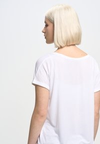 Vit t-shirt med kort ärm, lös passform, mjukt material och upprullade ärmslut. Baksidan har en rundad halsringning och subtila sömdetaljer.