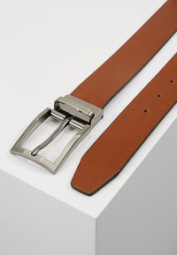 Ceinture en cuir marron avec une boucle rectangulaire en métal argenté brillant, présentant une texture lisse et plusieurs trous d'ajustement le long de la sangle.