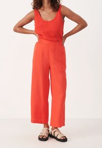 Oranje linnen tanktop met een ronde hals, gecombineerd met bijpassende wijde broek. Model draagt beige sandalen met bandjes.