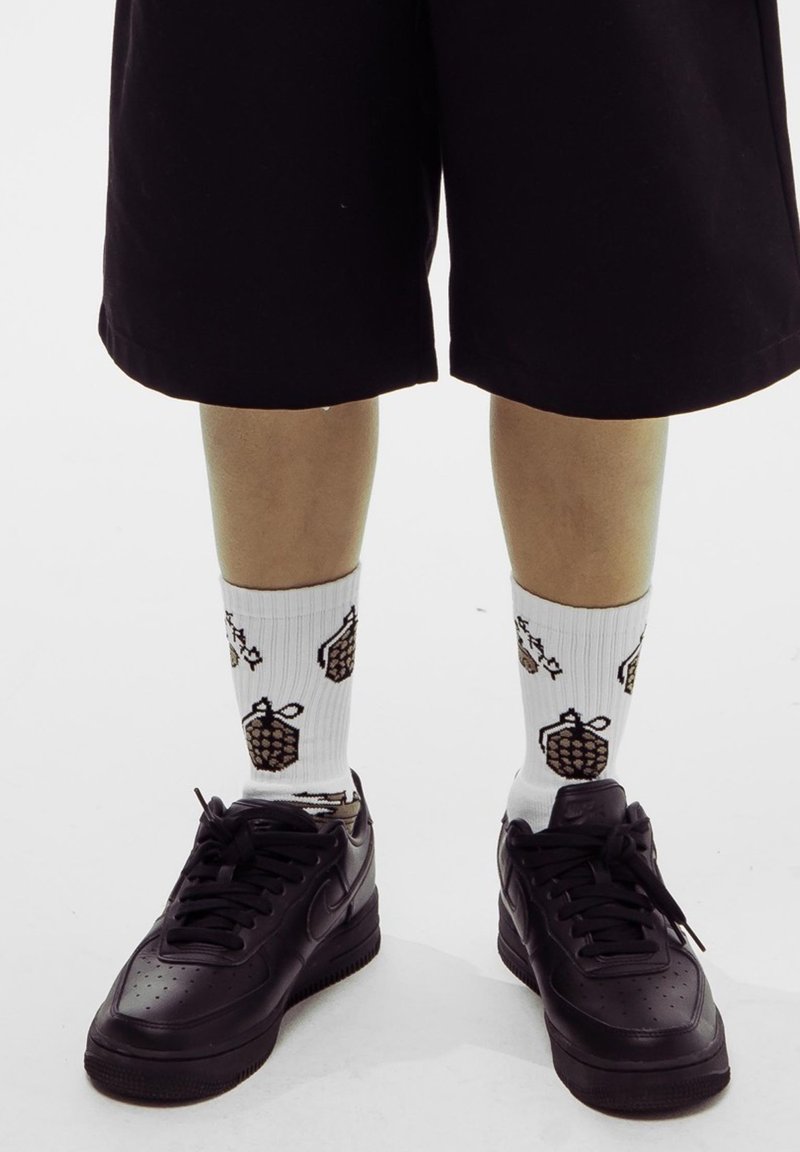 Zapatillas negras de Nike, calcetines blancos con estampado de piñas marrones y pantalones cortos negros hasta la rodilla. Textura suave y diseño casual.