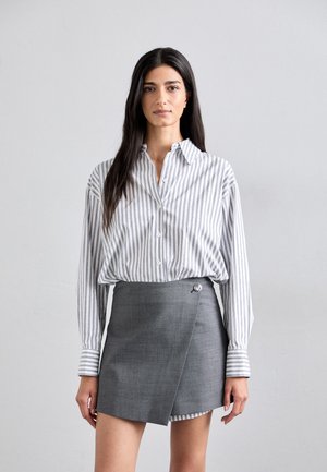 Chemise à rayures blanche et grise, associée à une jupe portefeuille grise avec un détail de bouton argenté. Tissu lisse, coupe décontractée.
