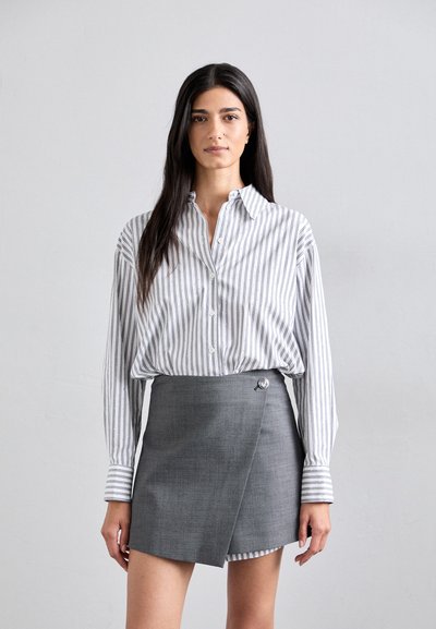 Gestreepte button-up blouse in wit en grijs, gecombineerd met een grijze wikkelrok met een zilveren knoopdetail. Zachte stof, ontspannen pasvorm.